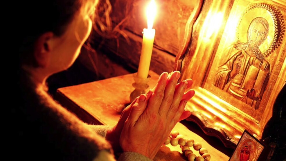 Человек тренируется креститься перед домашним иконостасом